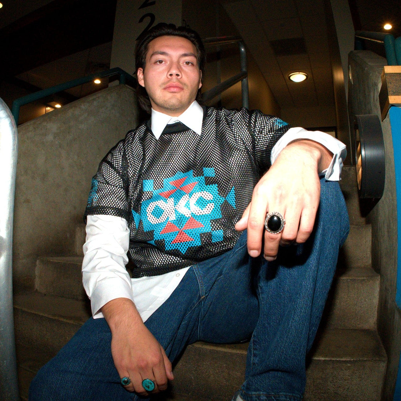 Man sitting on a staircase wearing a patterned sweater with a visible brand logo.