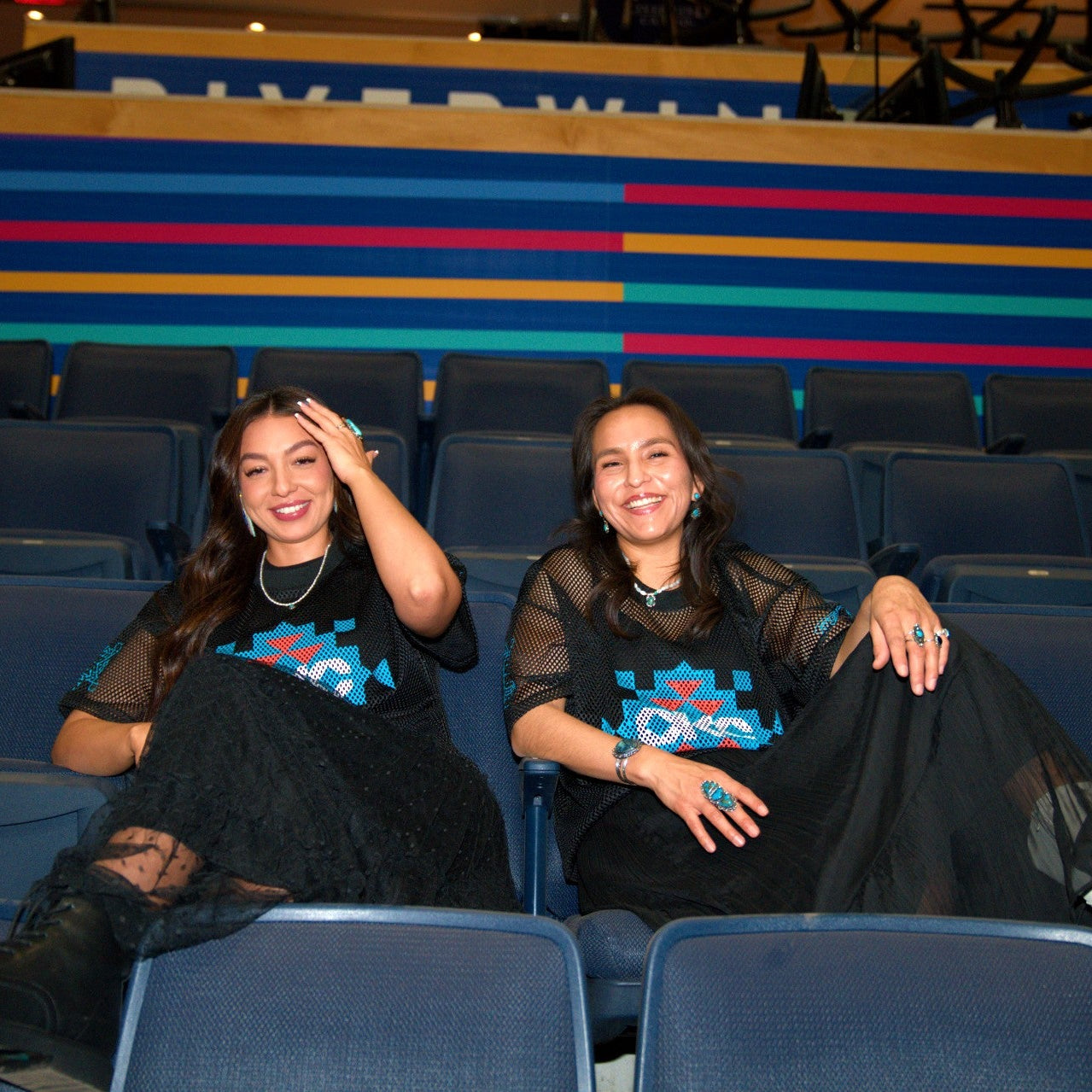 Two women sitting in a stadium with colorful seat backs