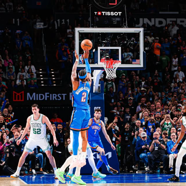 Basketball player taking a shot during a game with a crowd and advertisements in the background.